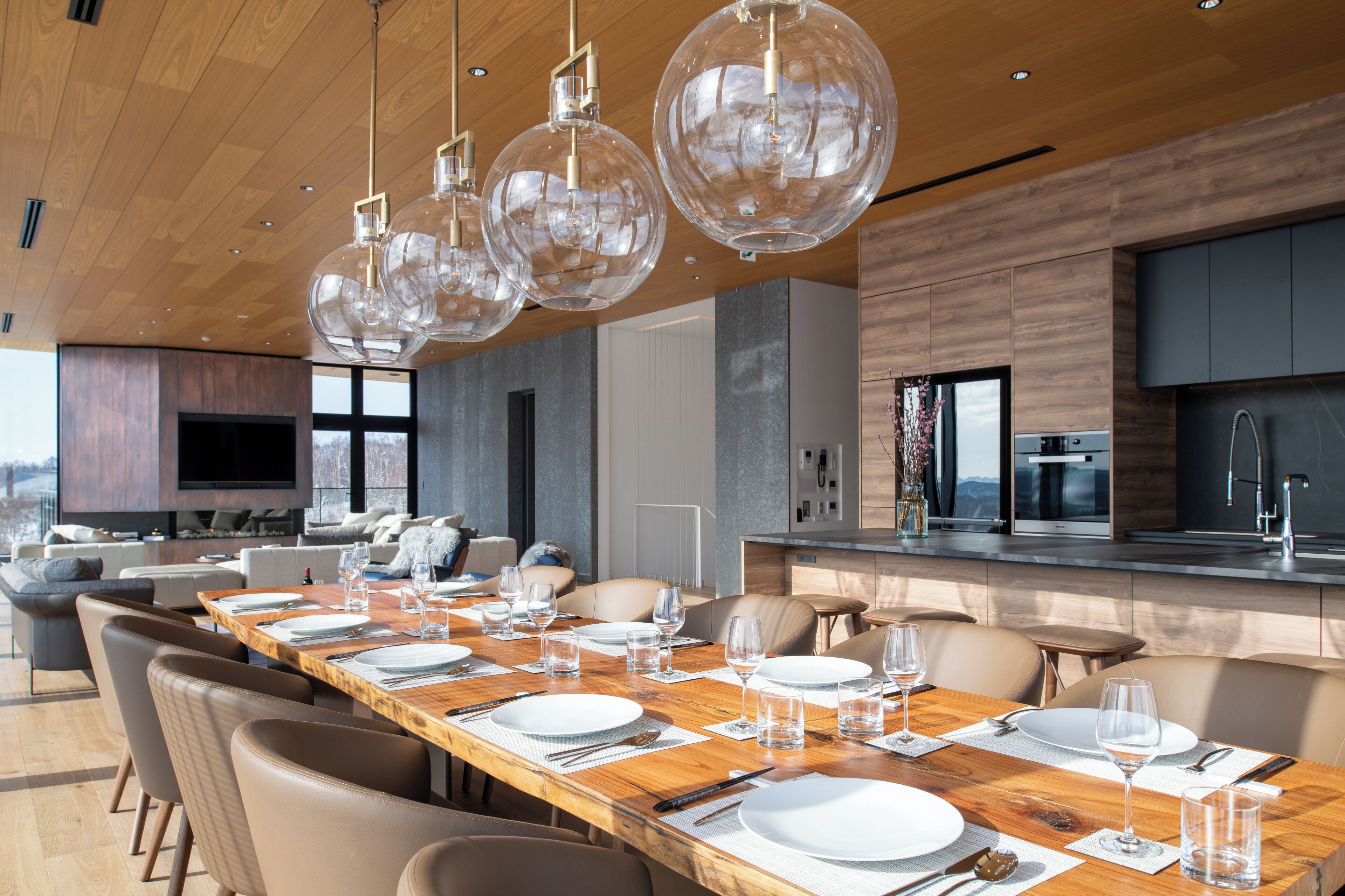 A modern dining area with a long wooden table set for a meal, surrounded by comfortable seating.