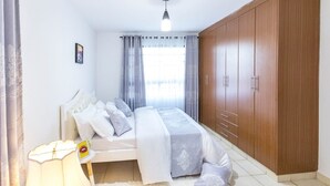 Ein Schlafzimmer mit Bett, Kleiderschrank, Nachttischlampe und einem Fenster mit Vorhängen.