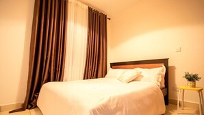 Ein ordentlich bezogenes Bett mit weißen Leinen, einem Holzkopfteil und einem kleinen Nachttisch mit einer Pflanze.