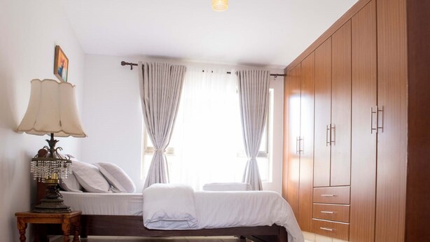 Ein Schlafzimmer mit Bett, Nachttisch mit Lampe, Kleiderschrank und einem Fenster mit Vorhängen.