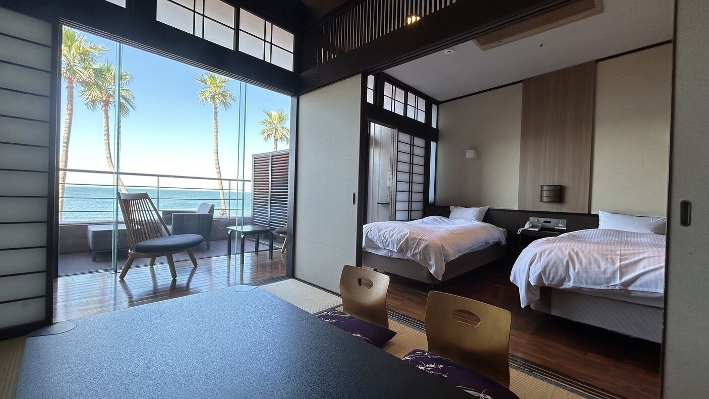 A modern hotel room with a balcony, two beds, a dining table, and a view of the ocean.
