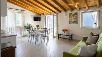 Ein Zimmer mit Holzboden, einem Essbereich mit Tisch und Stühlen, einem grünen Sofa und einem Gemälde an der Wand.