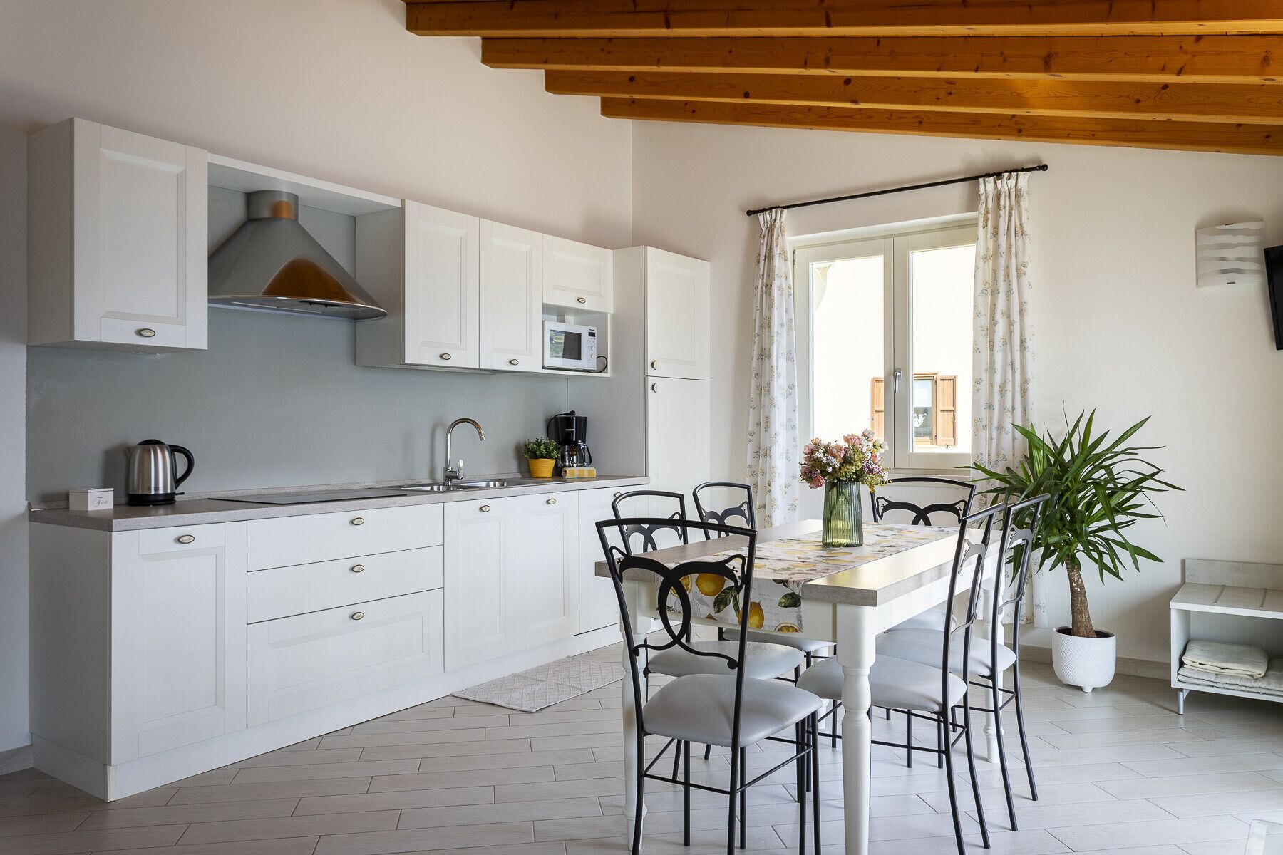 Eine moderne Küche mit weißen Schränken, einer Holzbalkendecke und einem Essbereich mit Tisch und Stühlen.