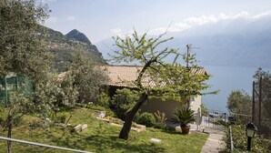 A house with a tiled roof, surrounded by a garden with various plants and a view of a mountainous landscape.