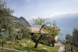 A house with a tiled roof, a garden with various plants, and a view of the sea and mountains in the background.