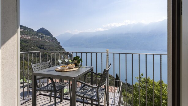 A balcony with a table, chairs, and a view of a lake and mountains.