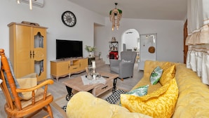 A living room with a yellow sofa, wooden chair, TV, and a wooden cabinet. - Villa Melita with heated pool in Biokovo Nature Park near Makarska (Zagvozd)
