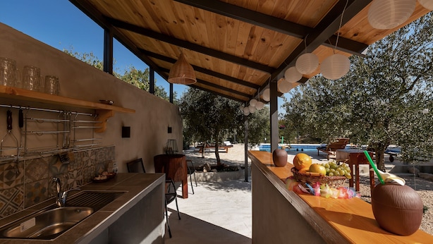 A modern outdoor kitchen area with a wooden pergola, a sink, and a counter with fruits and a decorative vase. - Villa Melita with heated pool in Biokovo Nature Park near Makarska (Zagvozd)
