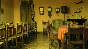 A dining area with wooden chairs and tables, a patterned floor, and wall-mounted clocks. - La Casa del Miedo (San Martin de Montalban)