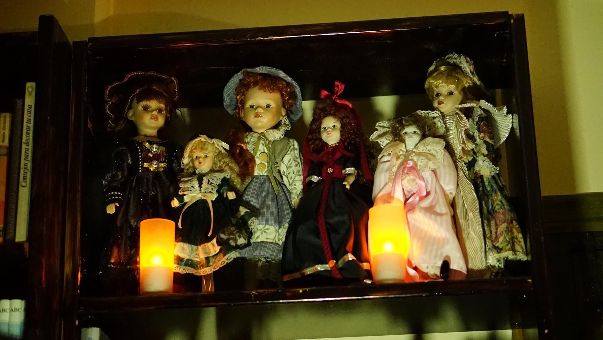 A display case with five dolls, each in different attire, and two lit candles.