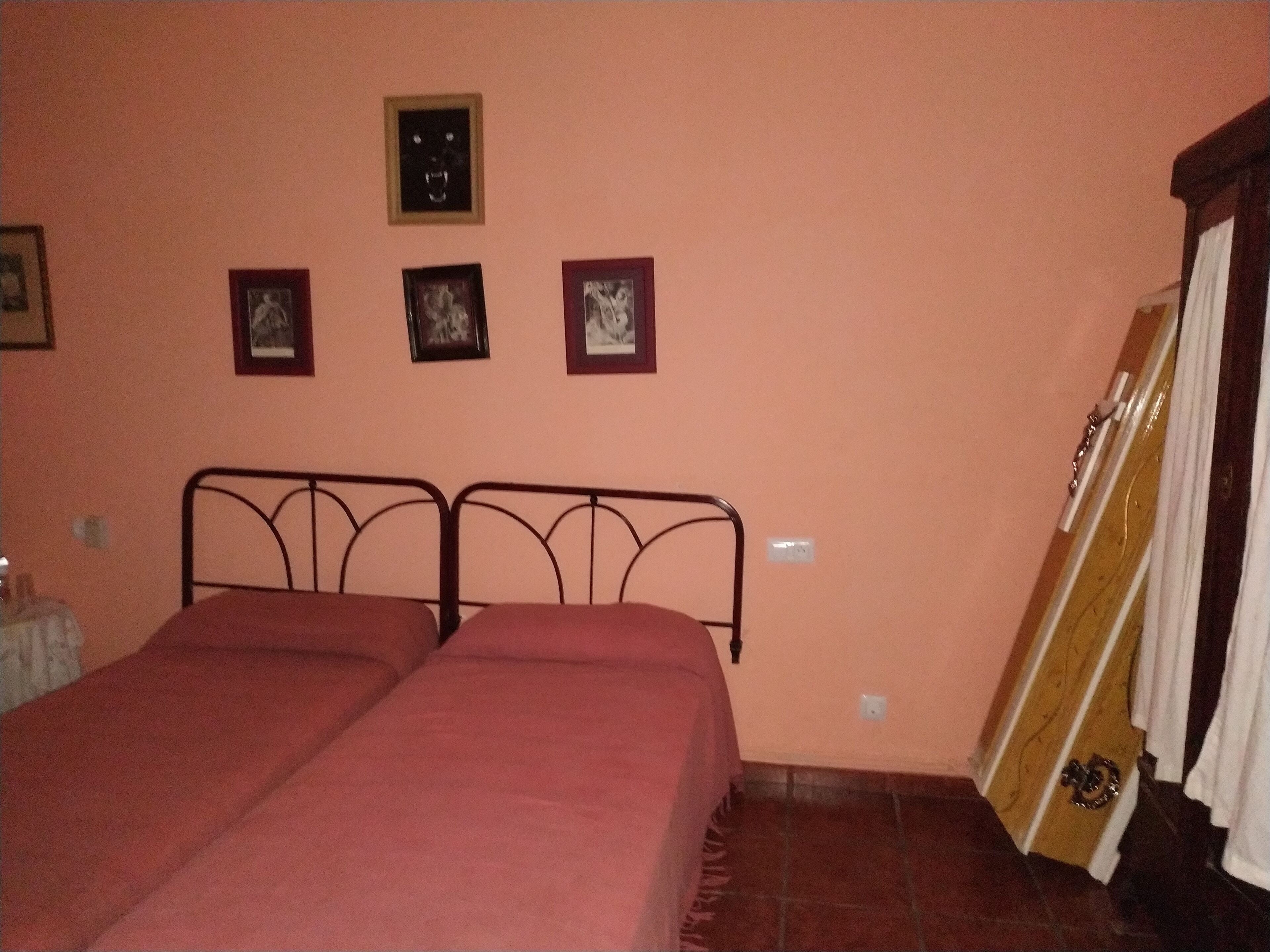 Un dormitorio con una cama doble, una puerta de madera con tirador de latón y tres cuadros en la pared.