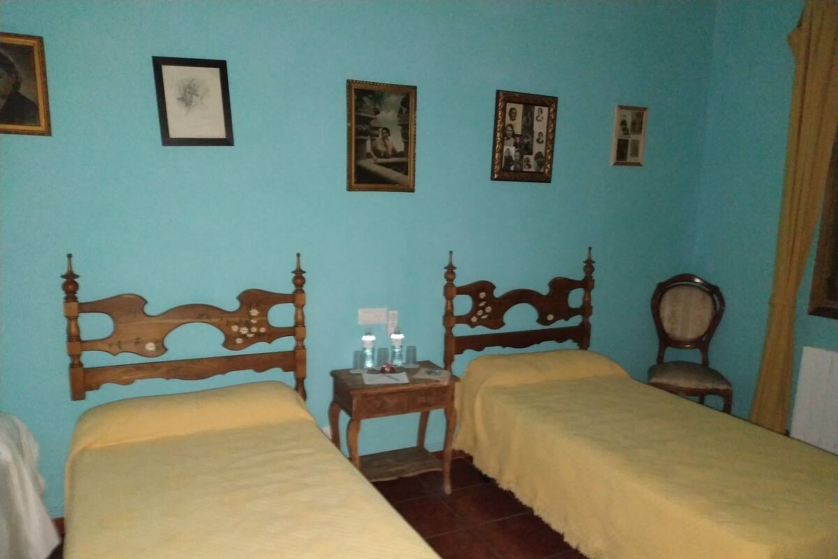 A room with two wooden beds, a small table with a lamp, and a chair.