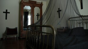 A bedroom with a bed, a wooden bench, a mirror, and a cross on the wall. - La Casa del Miedo (San Martin de Montalban)