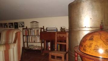 Una habitación con un globo terráqueo grande sobre un soporte, una estantería llena de libros, un sillón a rayas y un taburete de madera.
