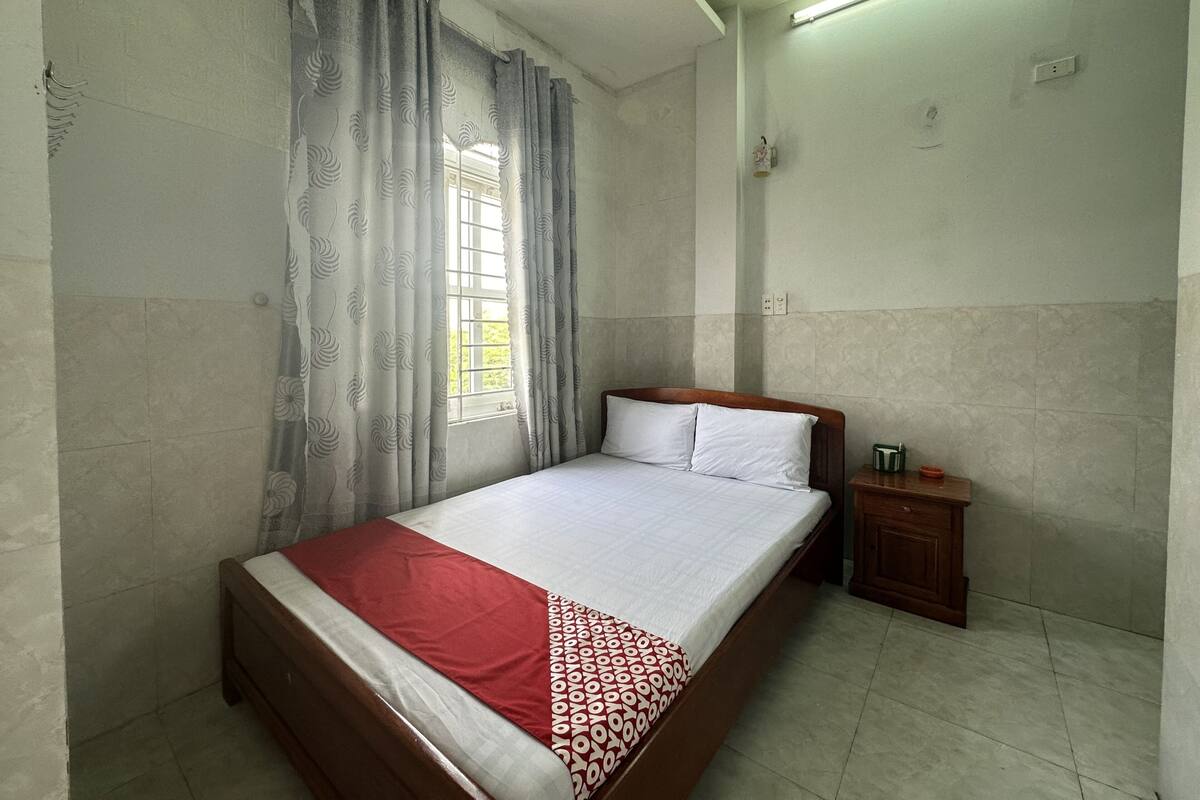 Un dormitorio con cama, cortinas, una mesita de noche y una ventana.