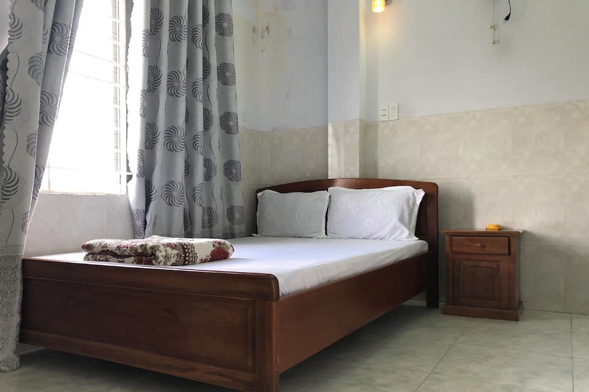 Un dormitorio con cama de madera, ropa de cama blanca, una mesita de noche y una ventana con cortinas estampadas.