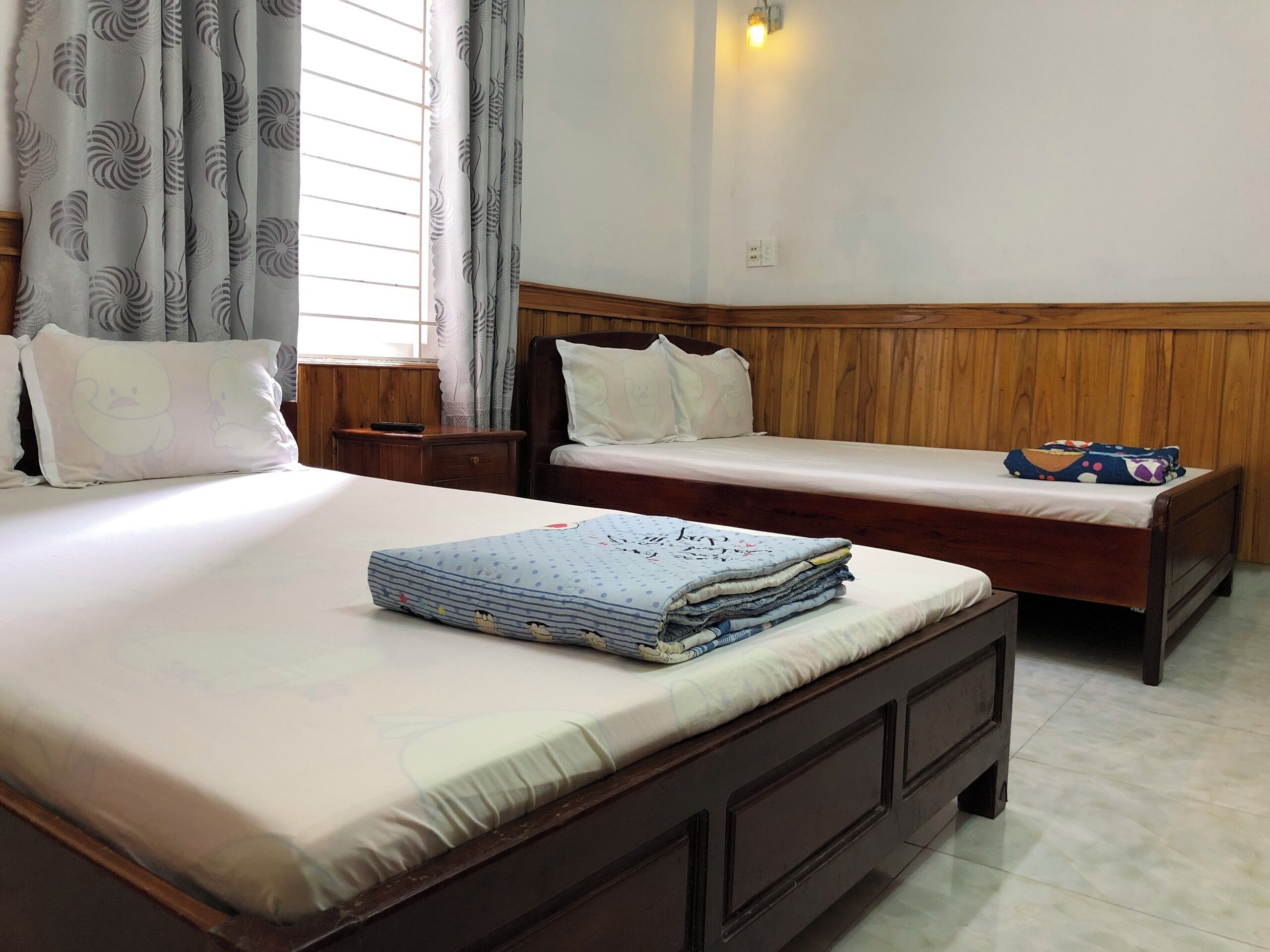 A double bed with a wooden headboard, a bedside table, and a window with curtains.