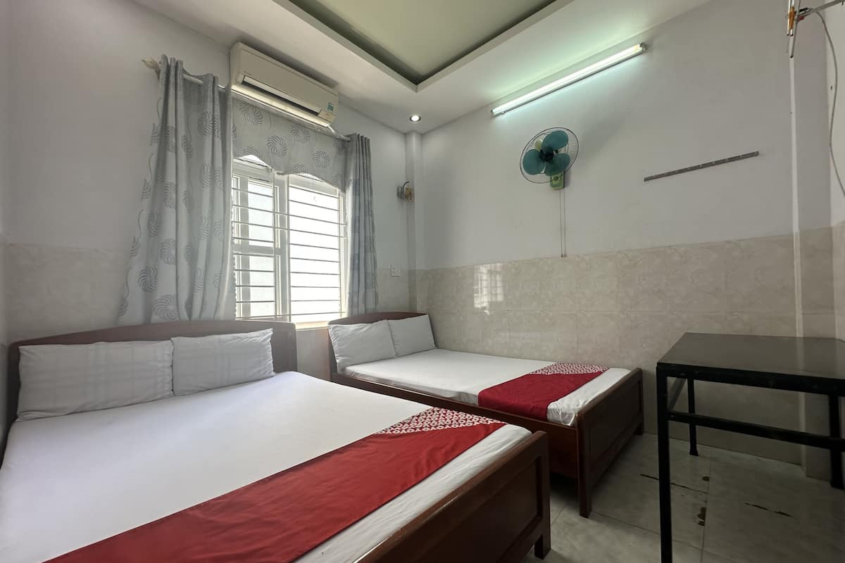 Habitación de hotel con dos camas, una mesa, aire acondicionado, ventilador de techo y ventana con cortinas.