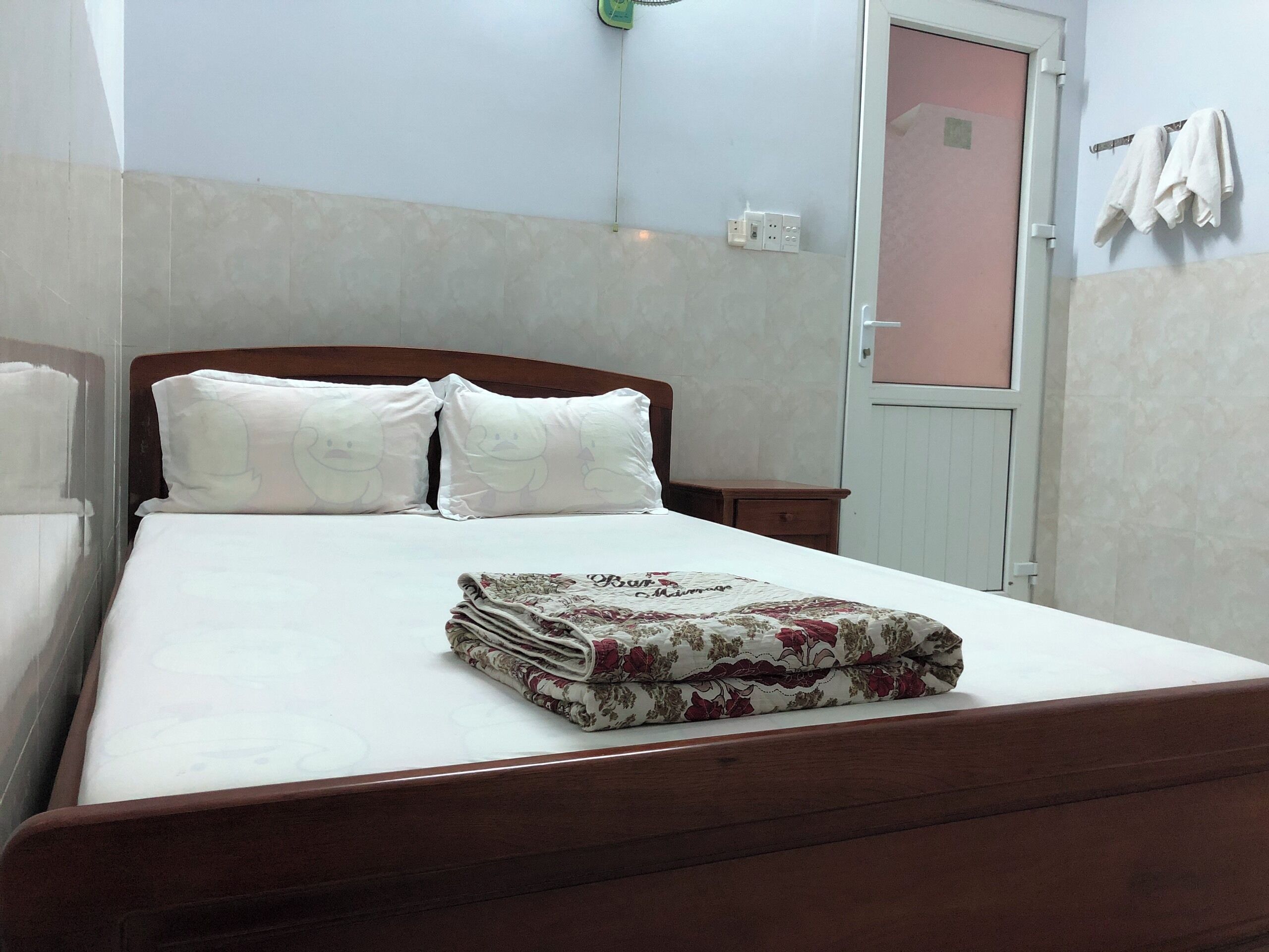 A neatly made bed with a floral blanket, a wooden headboard, and a bedside table with a lamp.