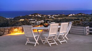 Un espacio al aire libre con mesa y sillas, con vistas a un pueblo costero al atardecer.