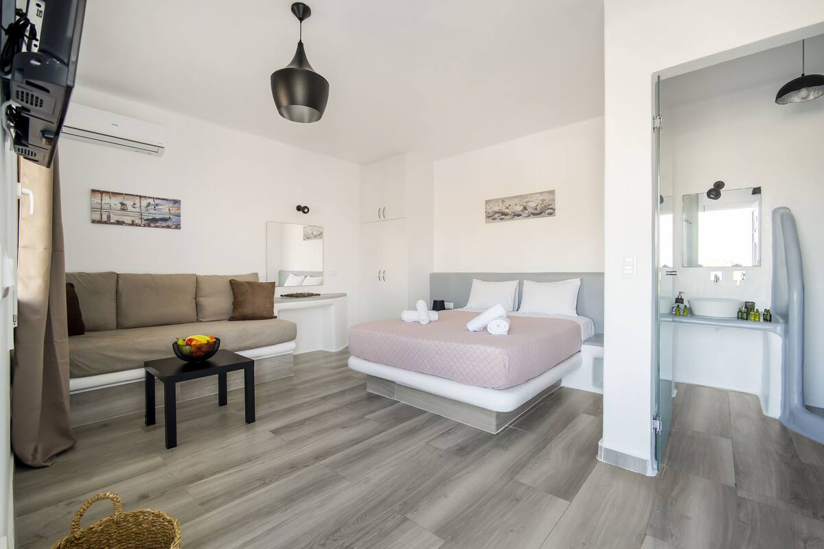 A modern hotel room with a bed, sofa, and a small table with a fruit bowl.