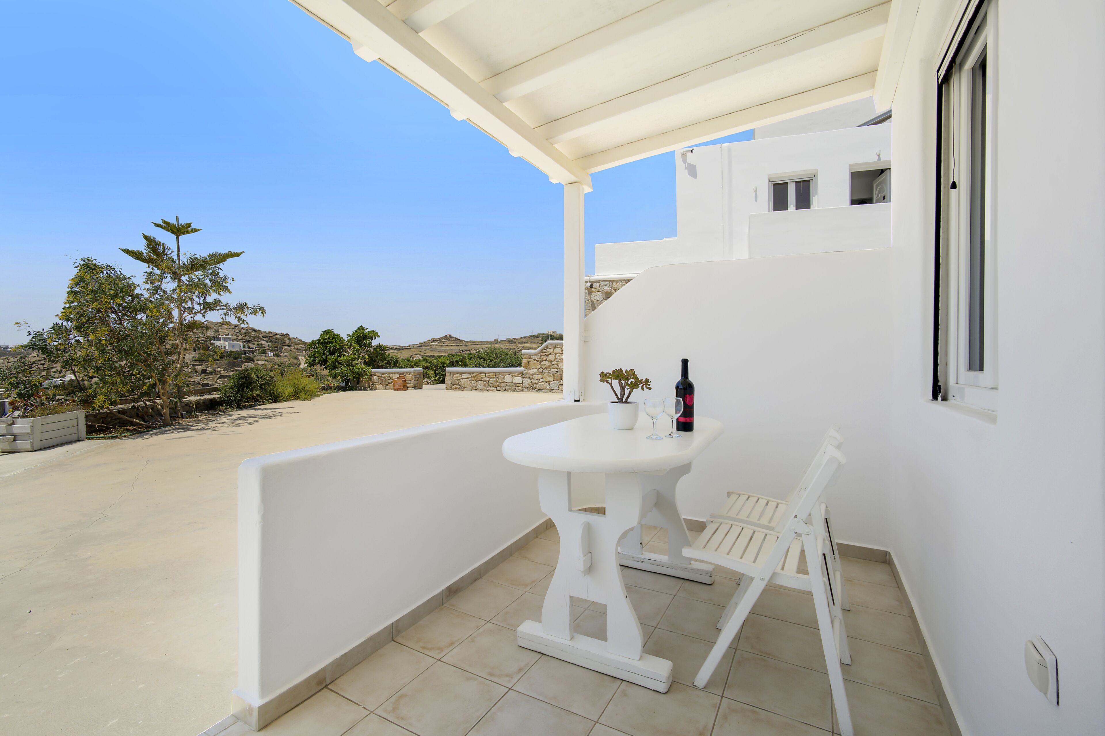 Un balcon blanc avec une table et des chaises, une bouteille et un verre.