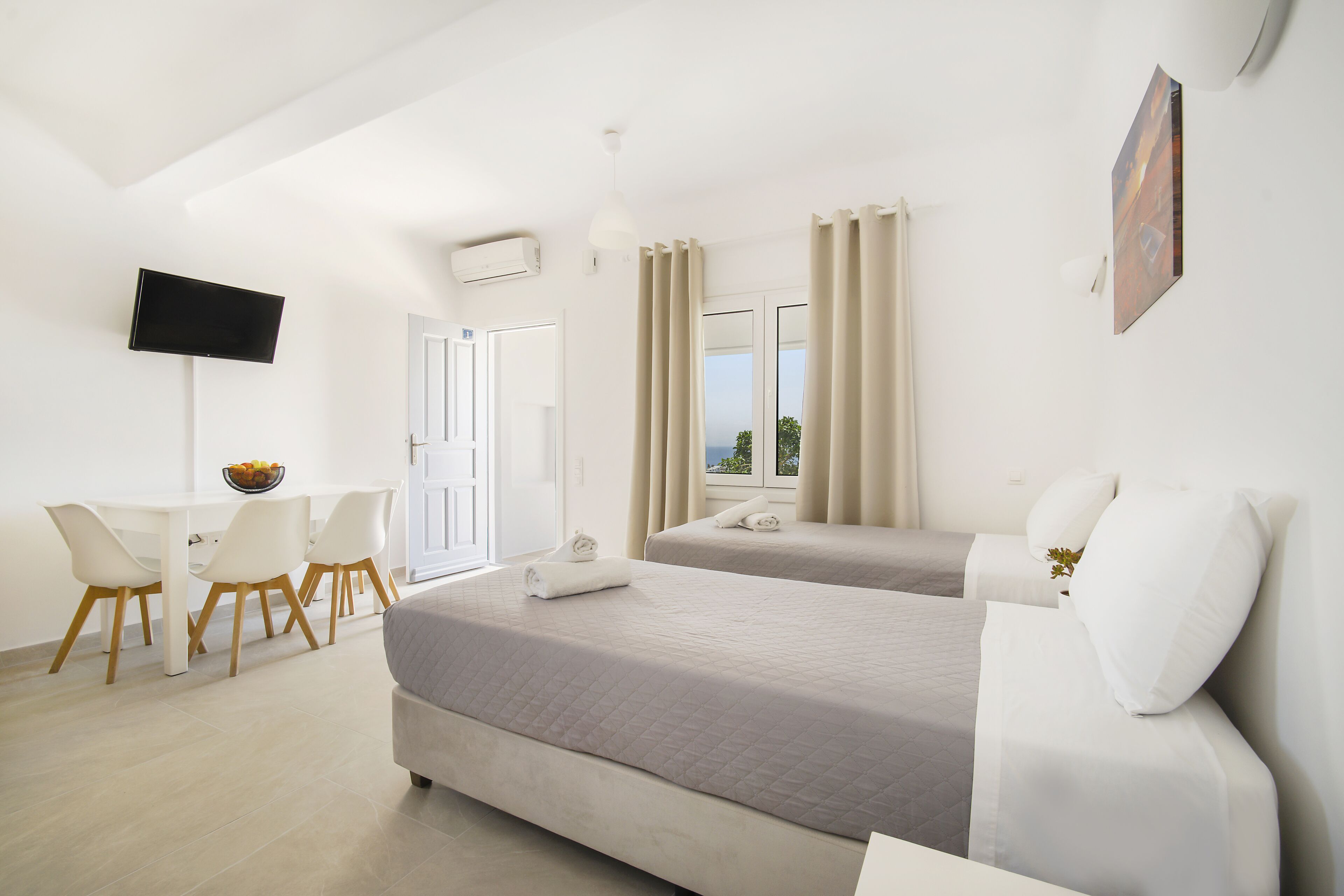 A hotel room with two beds, a desk with chairs, a TV, and a window with curtains.