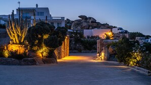 Paisaje desértico con un cactus grande, un edificio blanco y una camioneta blanca estacionada cerca de una puerta.