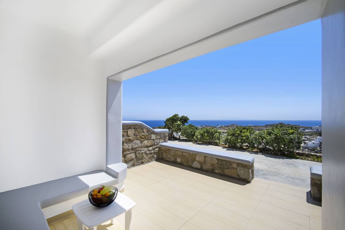 A balcony with a stone wall, a white bench, and a bowl of fruit.