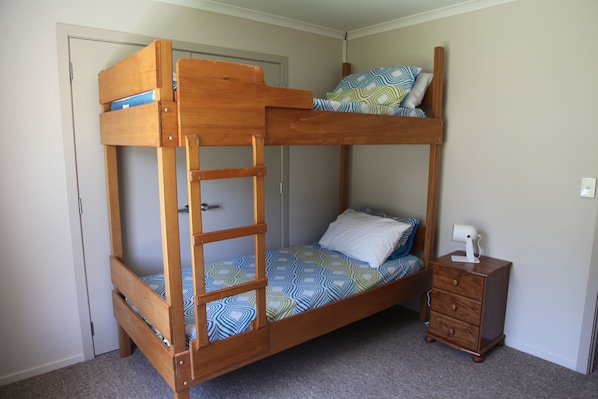 Een stapelbed met een ladder, een klein houten nachtkastje en een deur in een slaapkamer.