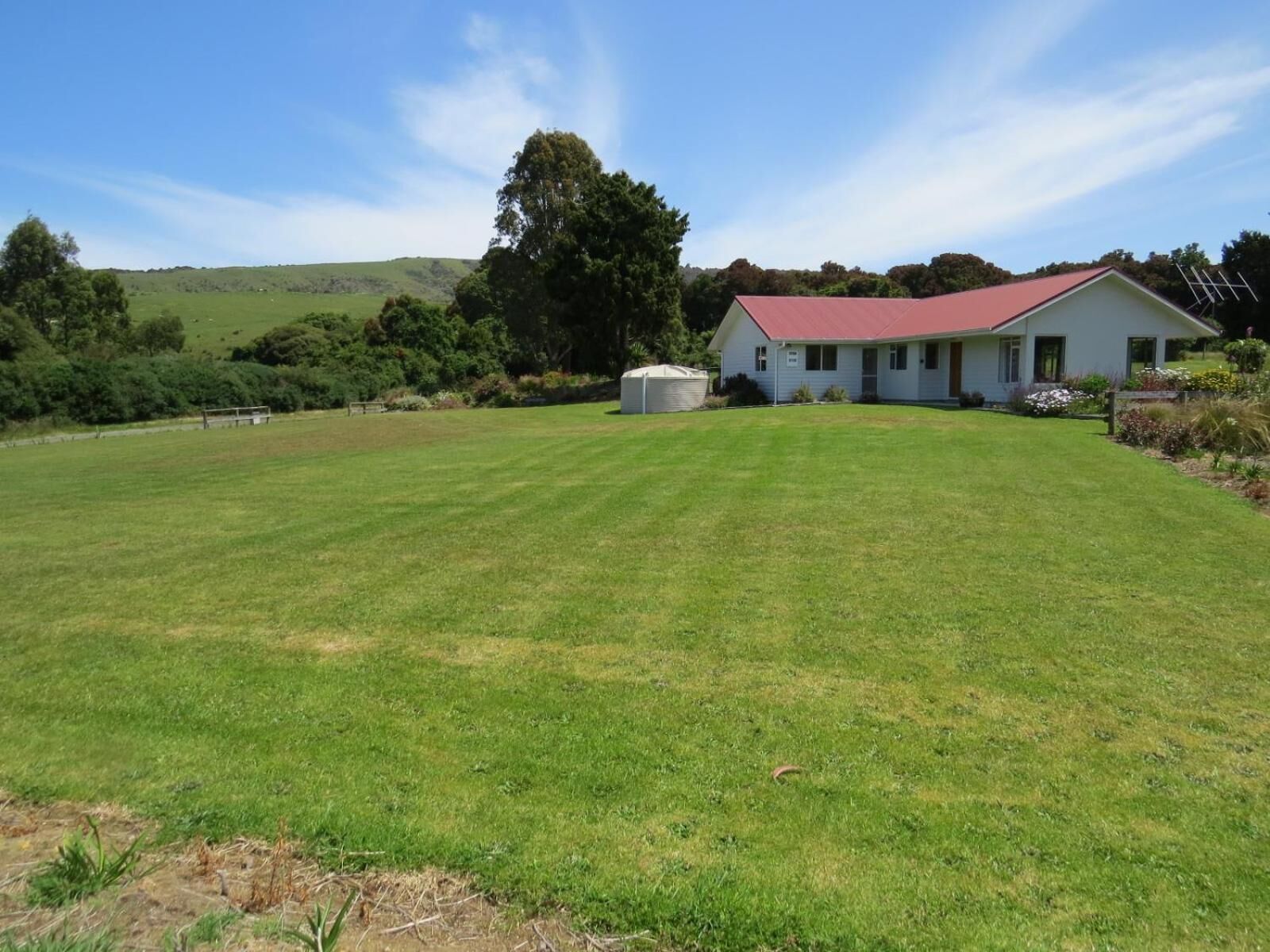 A single-story house with a red roof, surrounded by a well-maintained lawn and a few trees.