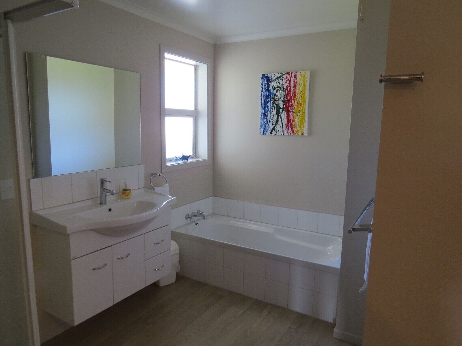 A bathroom with a white sink, mirror, and bathtub. There is a window with a view of the outside.