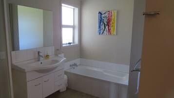 A bathroom with a white sink, mirror, and bathtub. There is a window with a view of the outside.