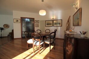 Un coin repas avec des chaises en bois et une table, un radiateur, des tableaux encadrés au mur et un meuble contenant des stylos.