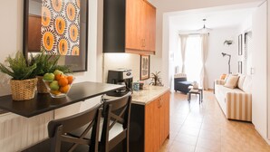 A modern kitchen with a dining area, featuring a coffee machine, a bowl of fruit, and a sofa in the living room. - Nephiria's Boho House with Acropolis View (Athens)