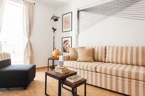 A living room with a striped sofa, a black armchair, a coffee table with books, a floor lamp, and artwork on the wall.
