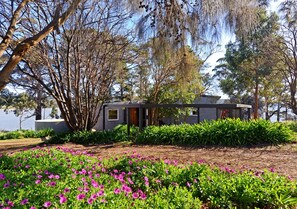 Une maison avec un jardin à l’avant, entourée d’arbres et bordée par un plan d’eau.
