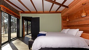 Un dormitorio con una cama grande, un banco y vistas al exterior a través de un ventanal.