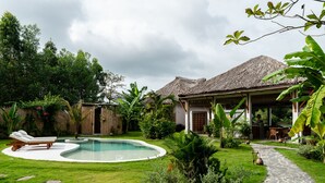 Een tropisch resort met een zwembad, ligbedden en een gebouw met rieten dak.