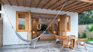 Een slaapkamer met een bed, nachtkastjes, een bedlampje, een hangmat en een eethoek met stoelen en een tafel.