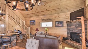 A log cabin interior with a fireplace, wooden walls, a sofa, and a dining area. - Rio Grande National Forest Cabin: Views & Hot Tub (Del Norte)