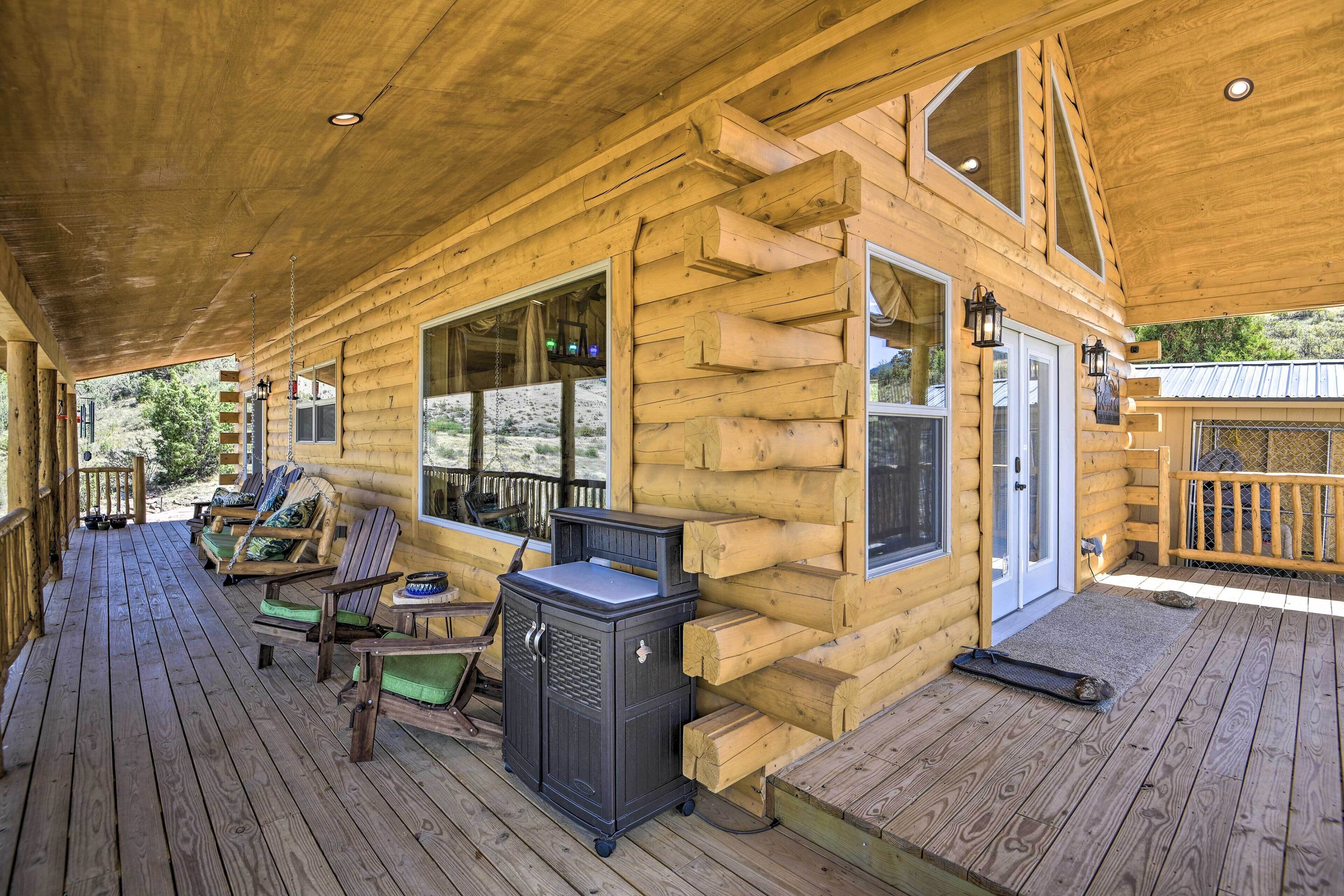 A log cabin with a wooden deck, outdoor seating, and a grill station.