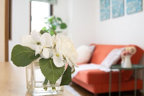 A clear glass vase with white flowers and green leaves on a wooden table. - Elle’s Shirokane guest house (Tokyo)