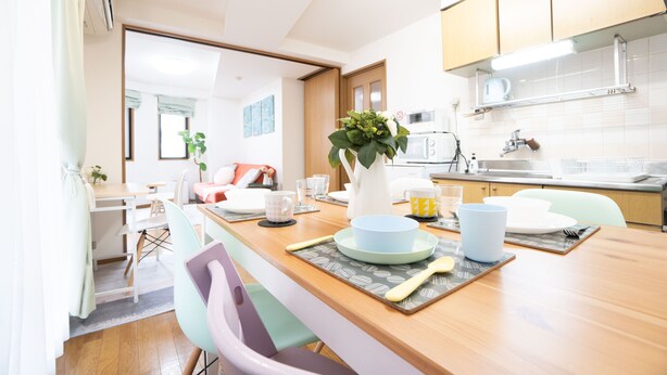 A modern kitchen with wooden cabinets, a dining table with chairs, and a kitchen island. - Elle’s Shirokane guest house (Tokyo)