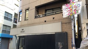 A building with a closed shutter, a sign for 'Minimal' on the ground floor, and a decorative banner on the right. - Elle’s Shirokane guest house (Tokyo)