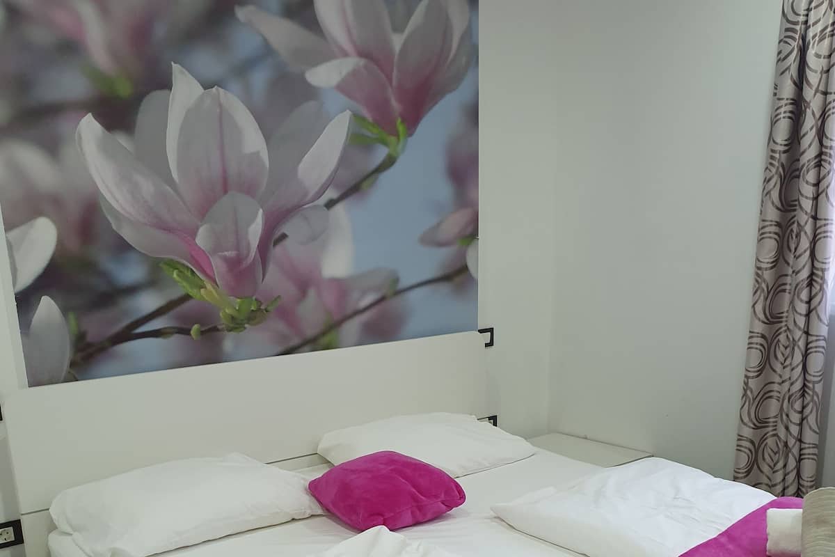 A neatly made bed with white linens and a pink blanket, a pink pillow, and rolled towels on the bed.