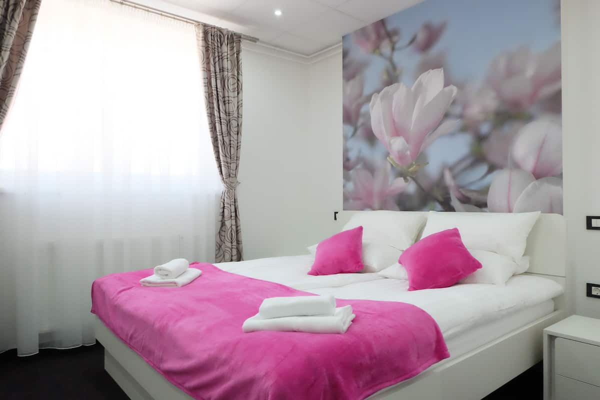 A bedroom with a bed, pillows, and a pink blanket.