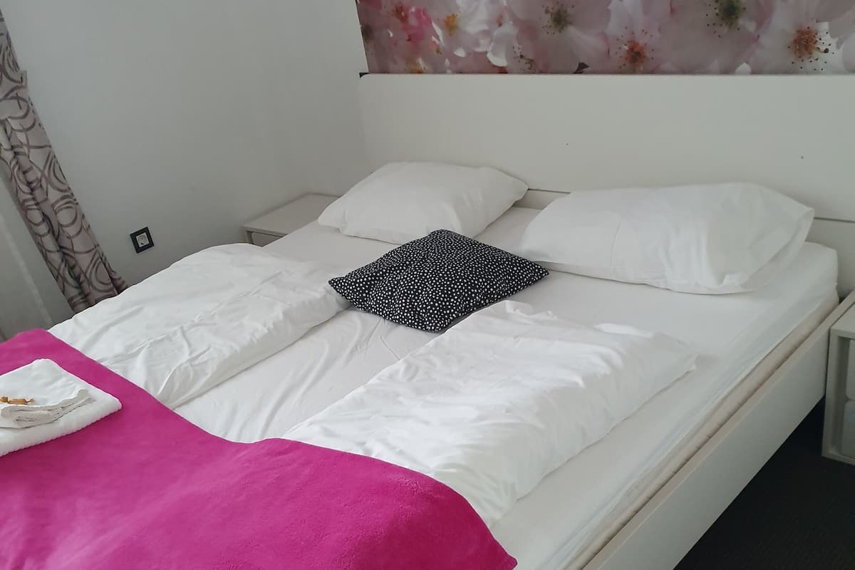 A bed with white bedding, a pink blanket, and a black and white pillow.