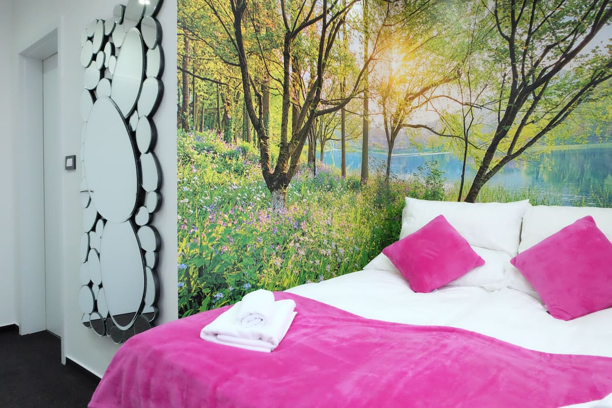 A bedroom with a large bed, white bedding, and a vibrant forest mural on the wall.