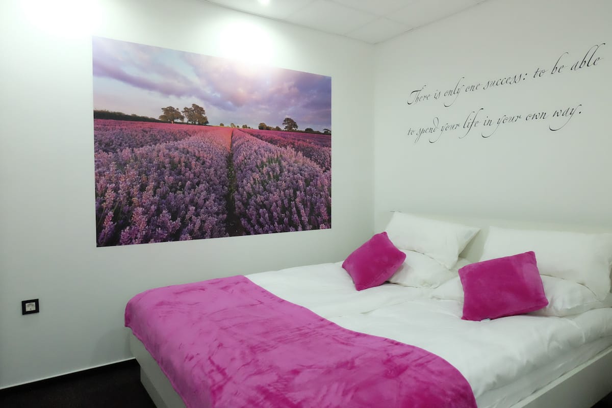 A bedroom with a bed, a large wall mural, and a motivational quote.